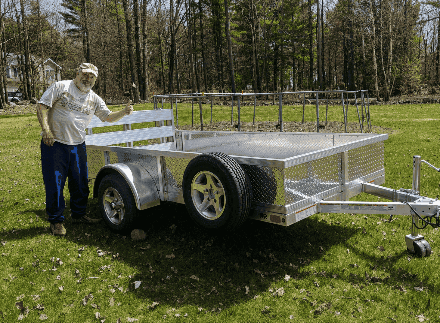 Customer standing beside a delivered Rugged aluminum utility trailer at a home.