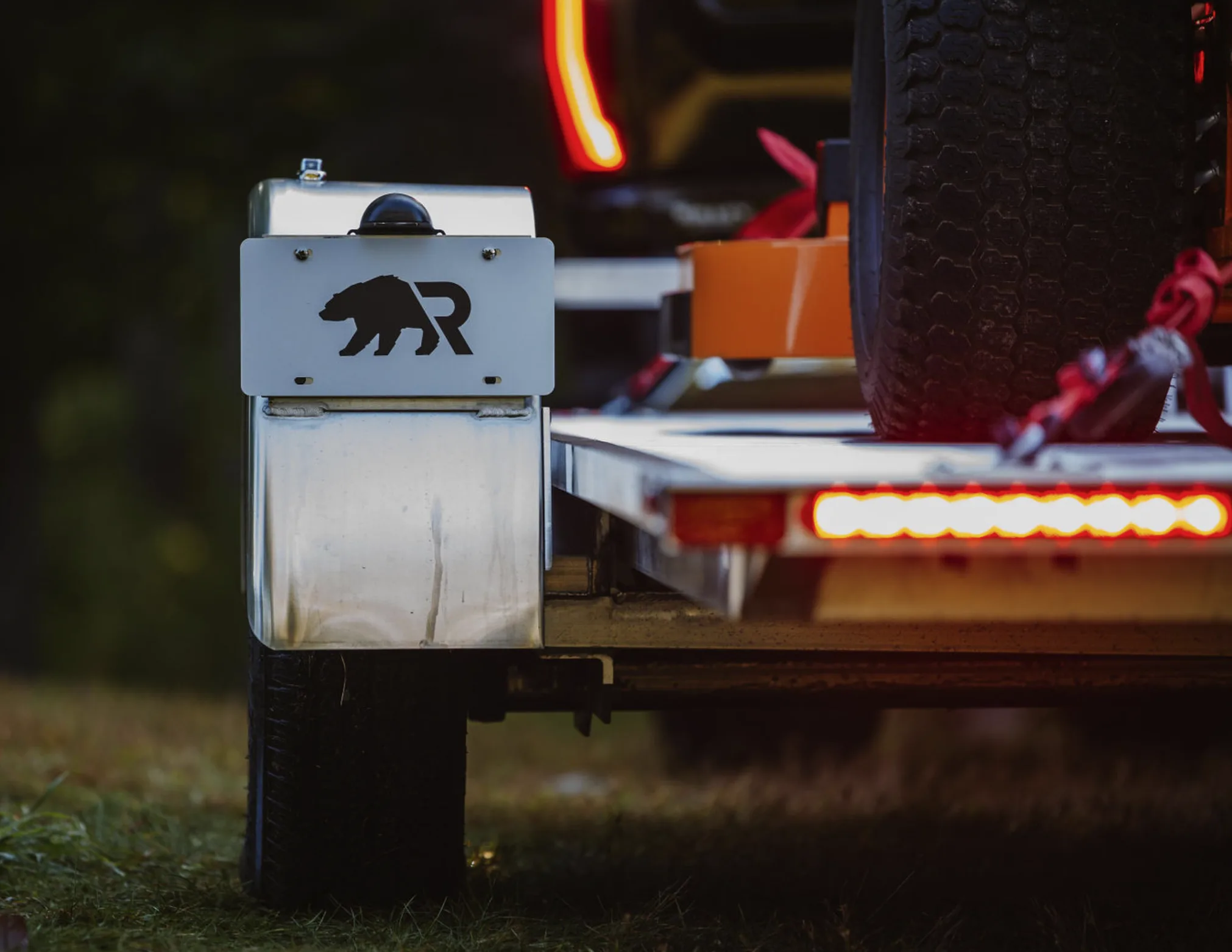 Rear corner of a loaded Rugged tilt trailer at dusk, showing the aluminum fender and welded frame edge