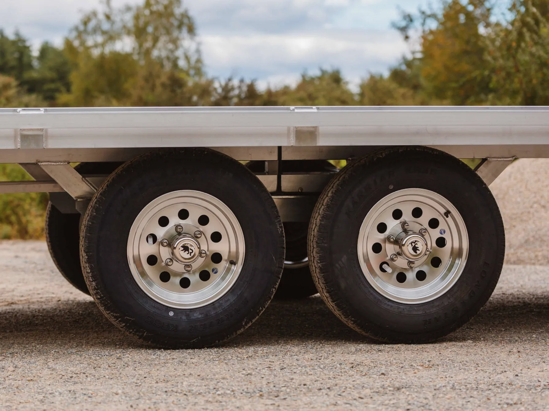 Tandem 15-inch six-lug aluminum wheels tucked beneath the flat deck of a Rugged deckover trailer