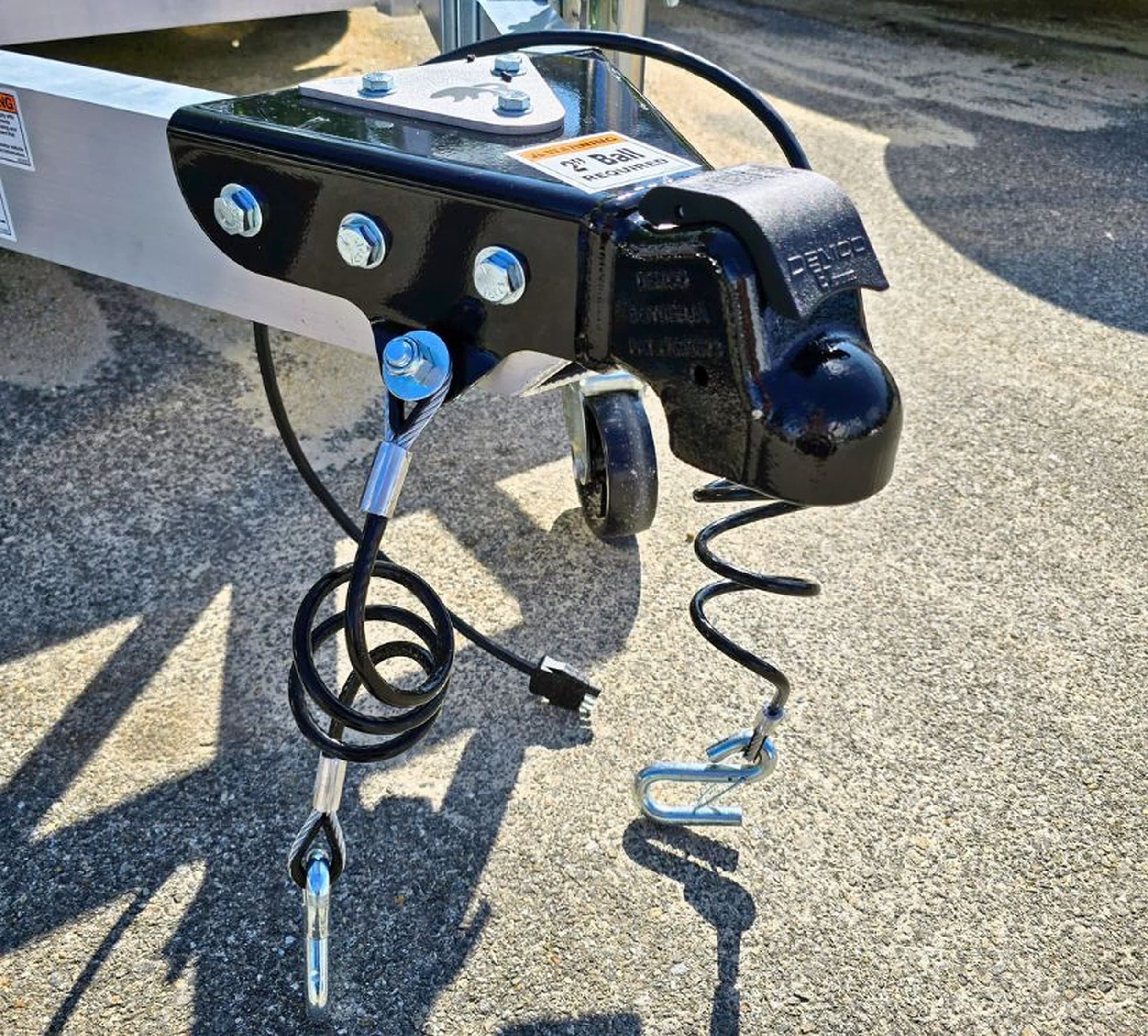 Close-up of the A-frame coupler, top-wind jack, and safety cables on a Rugged trailer tongue