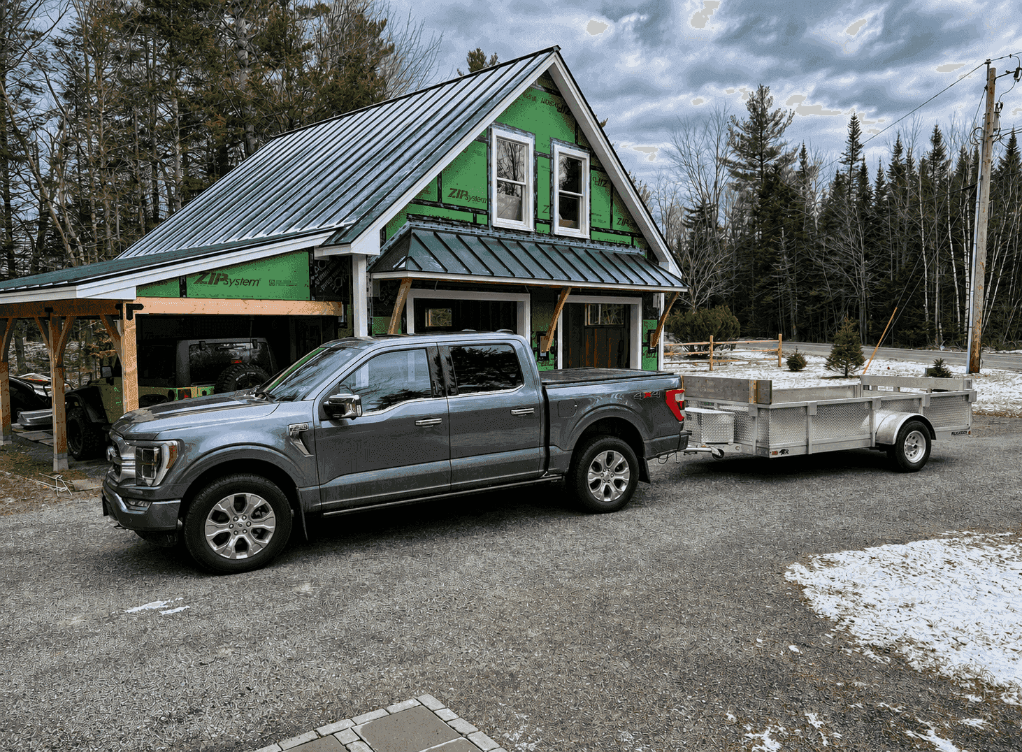 A gray pickup towing a Rugged all-aluminum utility trailer outside an active residential construction site.