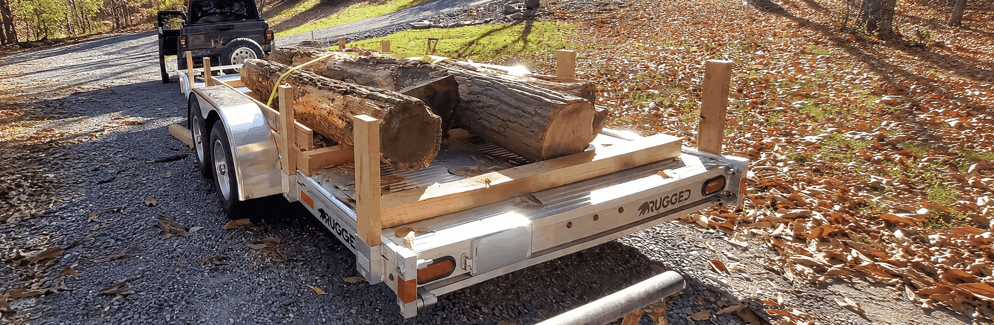 Rugged 6.5 × 18 tandem-axle utility trailer loaded with logs on a stake-side setup, hitched to a Jeep