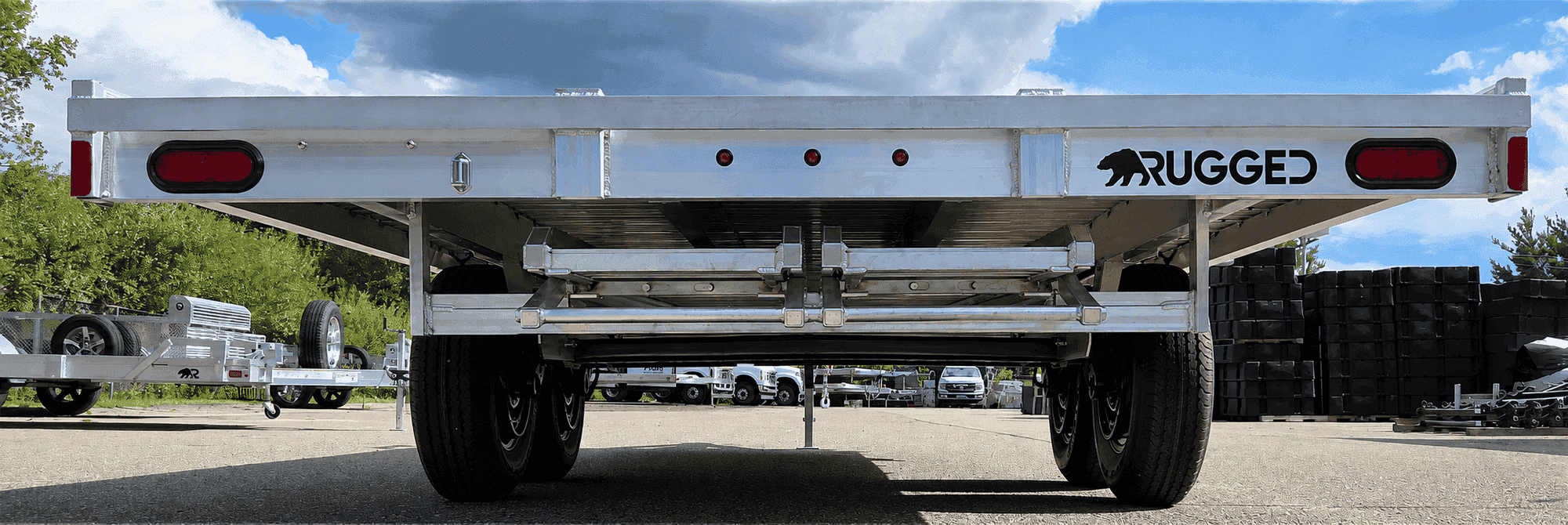 Rear view of a Rugged tandem-axle deckover trailer on the factory yard, deck and running gear visible