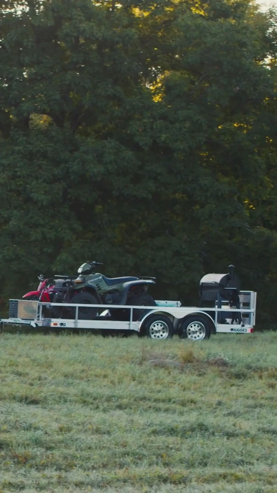 A pickup tows a branded Rugged all-aluminum trailer along an open mountain highway at golden hour.