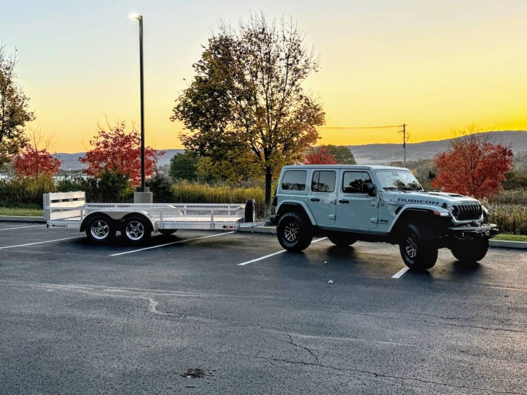 trailer with expanded metal side rails attached to a Jeep in a parking lot with a sunset behind it