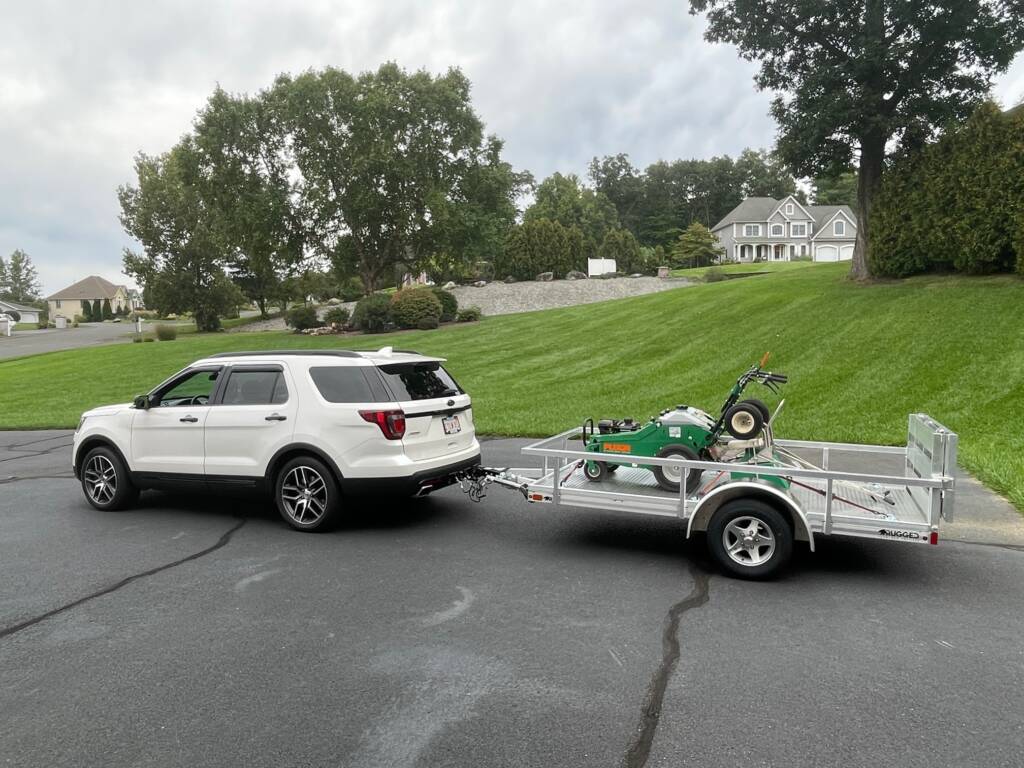 trailer with side rails attached to a car with lawn equipment in it